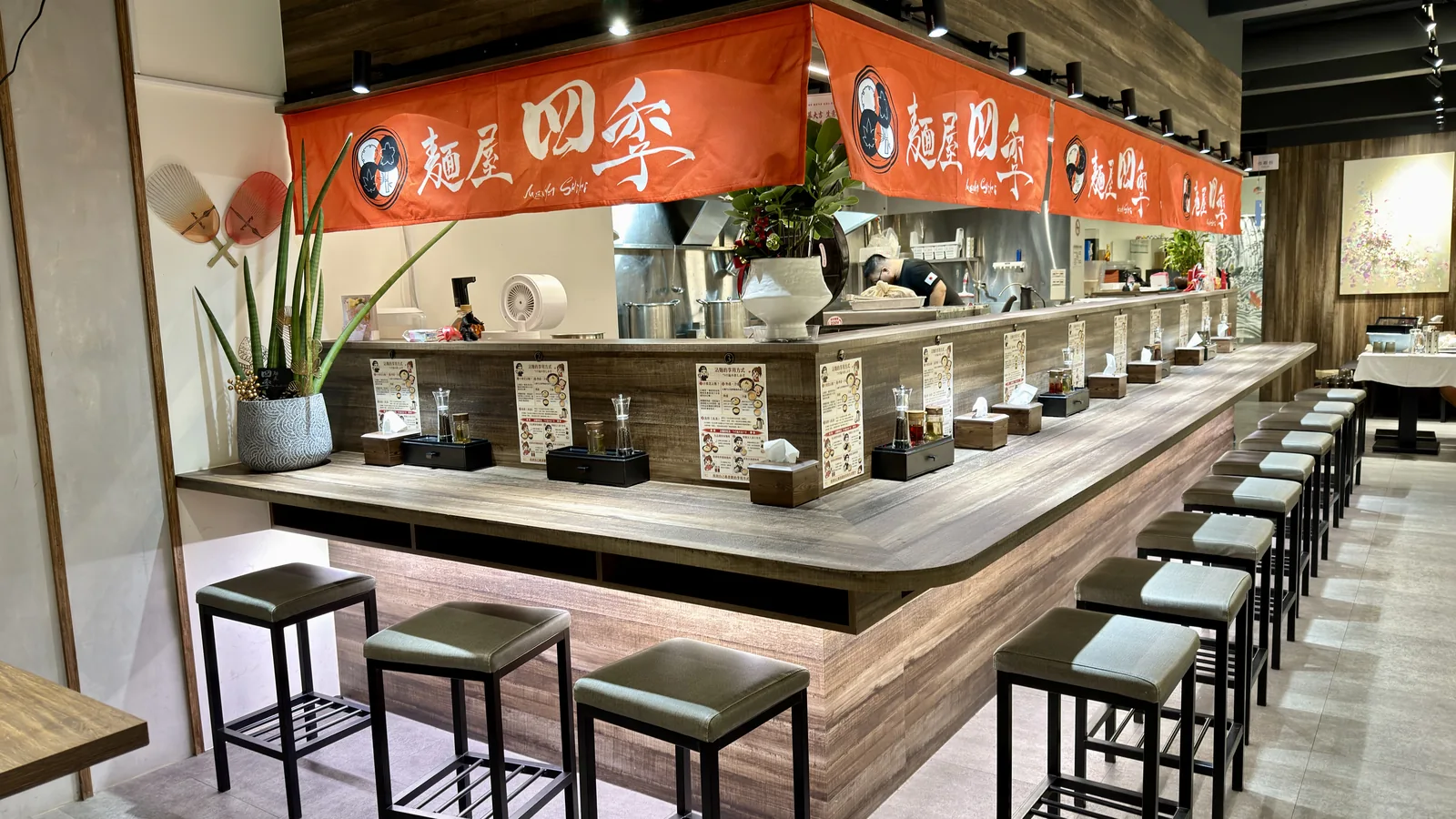 麵屋四季板橋店實景，橘色暖簾、木質吧檯與座位